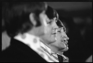 Paul McCartney, John lennon, and George Harrison during a Beatles press conference, in profile: Ringo Starr in foreground and John Lennon in the background
