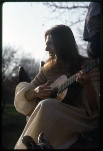 Judy Collins seated at the base of a statue, playing guitar