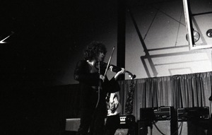 Unidentified band in performance in what appears to be a high school gymnasium: violinist