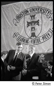 John Kenneth Galbraith (left) talking with presidential candidate Eugene McCarthy on dais at Boston University, in front of a large BU banner