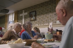 Church supper at the First Congregational Church, Whately: women seated at a table, whispering to one another, while eating supper