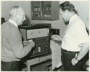 Dr. Chester Ellsworth Cross indoors talking with Carl Deubert, in front of a machine