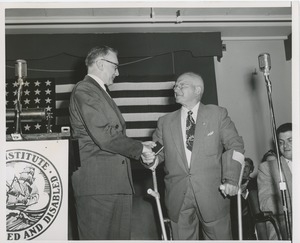 Unidentified man handing a gift to an older man with forearm crutches at an ICD event