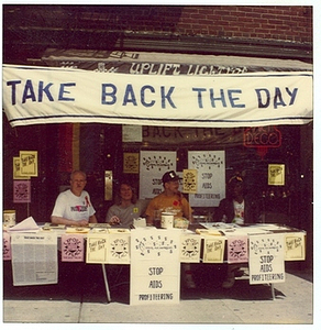 A Photograph of Marsha P. Johnson and Randy Wicker In Front of Uplift Lighting Under a Take Back the Day Banner