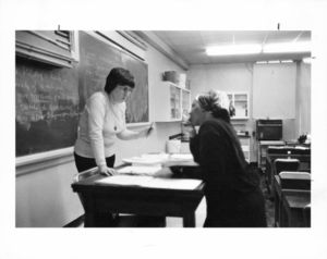 Suffolk University professor Beatrice L. Snow (Biology), standing behind desk in classroom, talking with a student