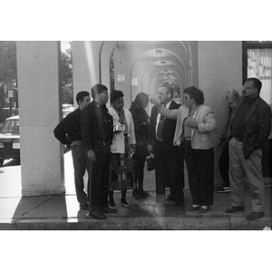 A group of men and women in business attire under the Villa Victoria arcade with a policeman.