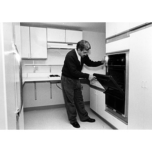 Carlos Luna opening the oven door in a newly-renovated kitchen.
