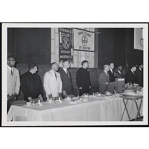 A man speaks at the head table while others stand during a Boys' Club Awards Night