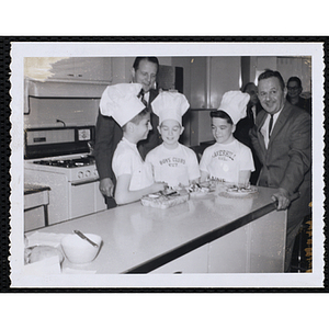 Members of the Tom Pappas Chefs' Club pose with plates of food in a kitchen
