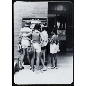 A group of girls stand at a candy vending machine