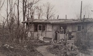 Two soldiers and one Red Cross worker in front of an abandoned bungalow
