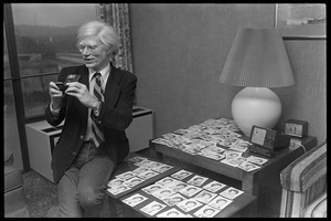 Andy Warhol seated with an array of polaroids at the Birmingham Museum of Art