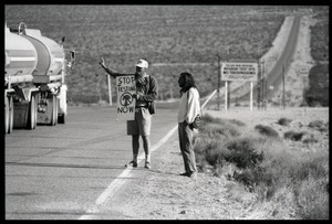 Activists flashing a peace sign at a passing truck by the road near entrance to the Nevada Test Site, holding a sign reading 'Stop testing now': Nevada Test Site peace encampment