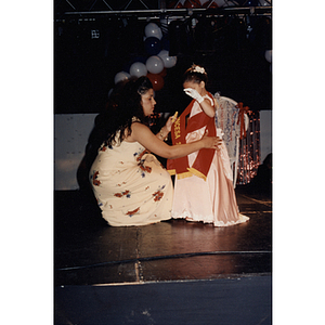 A woman puts a second sash on a little girl on stage during the Festival Puertorriqueño