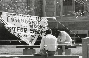 Boston College students sitting outdoors near Festival of Friendship banner. Festival of Friendship is a Boston College organization founded in 1982