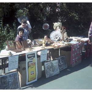 Three women smiling and selling decorative arts and crafts at tables at a Latino street festival