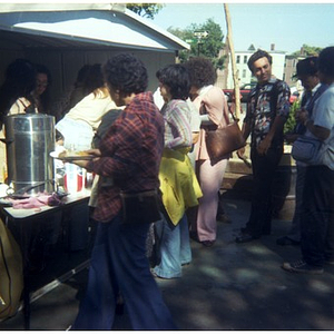 Seven Hispanic American people stand in line and wait to buy food at a Latino street festival, with four people serving them