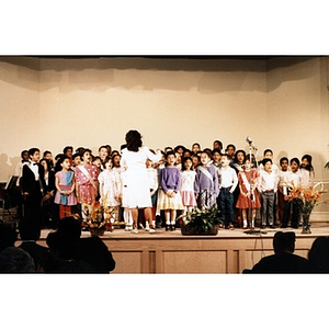 Woman conducting a group of children who are singing on stage at the Jorge Hernandez Cultural Center.