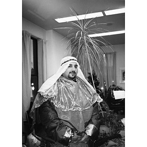 Man dressed as one of the Three Kings, or Magi, poses for a portrait in front of the office palm tree.