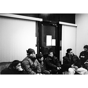 Boys sitting in an indoor space wearing coats and hats.