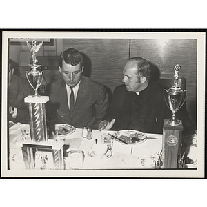 William O. Taylor II, Overseer of the Boys' Clubs of Boston, seated with a priest at a Boys' Club sports awards event