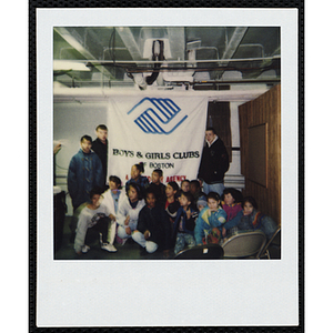 Seventeen boys and girls posing with the Boys and Girls Clubs of Boston banner, some of them looking up to their right, during an event at the Chelsea Clubhouse