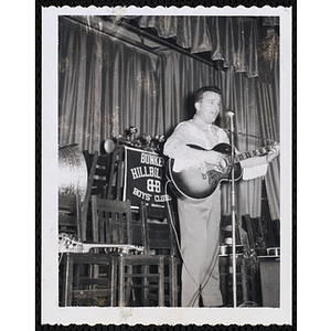 A man plays an acoustic guitar on stage at a Bunker Hillbillies event