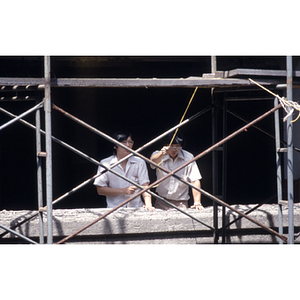 Two men stand on a balcony beside some exterior scaffolding