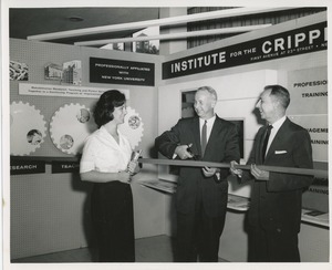 Two unidentified men cutting a ribbon next to an unidentified woman holding books in front of an ICD exhibit