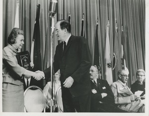 A woman holds the 1966 President's Trophy and shakes Hubert Humphrey's hand