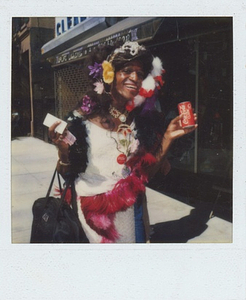 A Photograph of Marsha P. Johnson Wearing a White Dress and Feathered Accessories, Holding a Coca-Cola Can