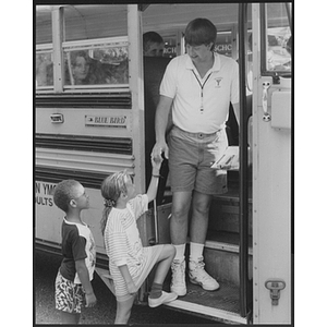 Young Men's Christian Association coach helping young children onto a bus