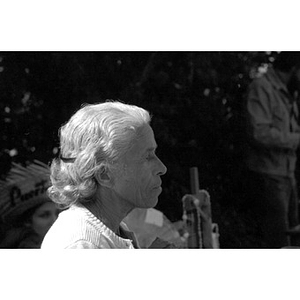 Head-and-shoulders profile of an older Hispanic woman with white hair, facing right, at a Latino street festival