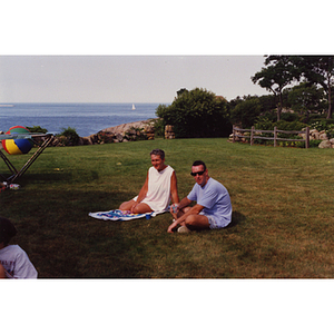 A woman and a man sit in a field with the ocean in the background at a Boys & Girls Club Board outing