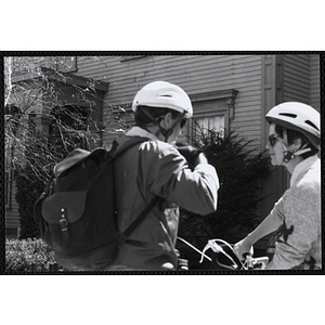 A man, facing away from the camera, puts a helmet on while a woman waits on her bicycle during the Boys and Girls Clubs of Boston 100th Anniversary Celebration Street Fair