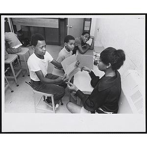 A boy shows his drawing to an art instructor while two others look on at the Boys' Clubs of Boston