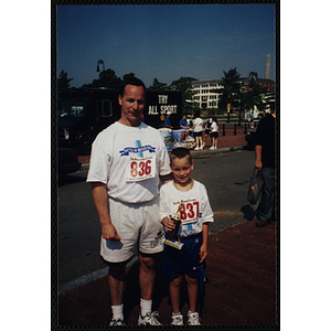 A boy holding a trophy poses with a man at the Battle of Bunker Hill Road Race