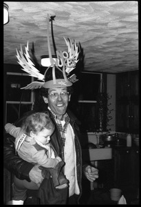 Dan Keller, making a silly face, wearing a winged No Nukes headdress, holding a baby, Montague Farm commune