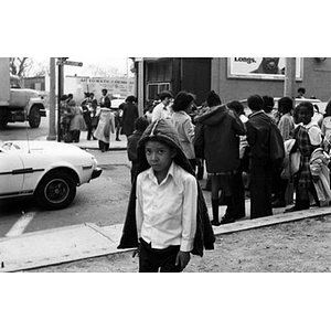 Hispanic American boy stands on the corner of Dudley Street and Mt. Pleasant Avenue, just outside of La Alianza Hispana headquarters in Roxbury, Mass., while groups of children congregate behind him