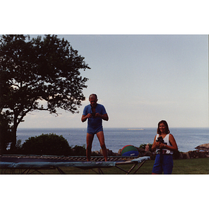 A man looks into his camera standing on a trampoline, while a woman stands beside him and holds her camera, during a Boys & Girls Club Board outing