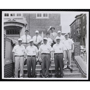 Group portrait of ten men standing on the stairs, wearing short sleeve shirts with the Kiwanis Club logo