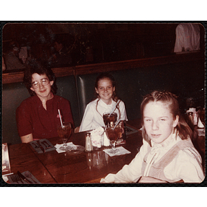 Two girls and a boy, seated at a table, smile for the camera during a Charlestown Boys & Girls Club event