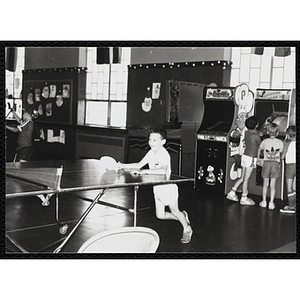 A boy leans against a table tennis table in a hall