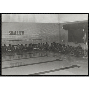 A group of boys sit at the edges of a natorium pool