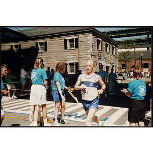 A runner crosses the finish line as race officials cheer him on during the Battle of Bunker Hill Road Race