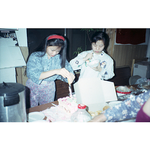 Two girls serve and eat cake at a Chinese Progressive Association holiday party