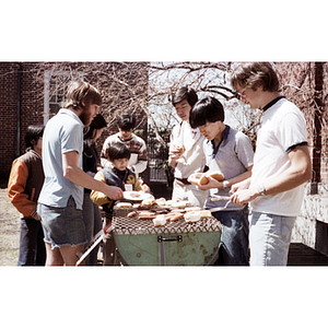 Group gathers around a grill to claim hamburgers and hot dogs