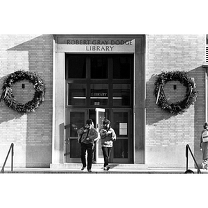 Two students exit Dodge Library which is decorated for the holiday season with two wreaths
