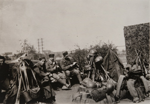 Five soldiers on a bench alongside kits, helmets and bayoneted rifles