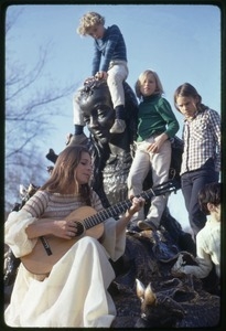 Judy Collins seated at the base of a statue, playing guitar for children